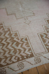 Vintage Oushak rug section showing distressed pale pink pile, bronze geometric, and floral border.