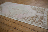 Vintage distressed Oushak rug corner, showing pale pink and beige floral border with textured pile.