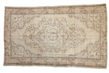 Vintage distressed Oushak carpet with faded ivory, peach, and charcoal floral medallion. 5'7