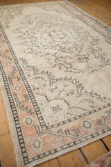 Distressed Oushak rug: faded ivory field with even wear and a soft apricot border.