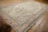 Distressed Oushak rug corner: worn ivory pile, peach border, and charcoal patterns.