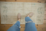 Distressed vintage Oushak runner, showing textured wear, ivory field, and faded dusty green patterns.