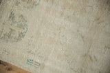 Distressed texture of vintage Oushak rug in ivory, revealing wear and faded green designs.