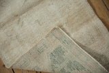 Distressed hand-knotted ivory pile of an Oushak rug, showing its striped green and pink foundation.