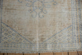 Decorative distressed Oushak rug corner, showcasing beige texture and faded blue geometric motifs.