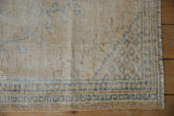 Distressed Oushak rug, showing beige field, blue geometric border, worn pile, and fringe.
