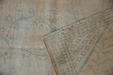 Distressed vintage Oushak rug, showing its worn beige pile and reverse side's blue lattice pattern.
