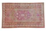 Distressed vintage Oushak rug with bubblegum pink medallion, beige field, and terracotta borders.