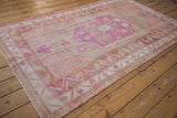 Distressed Oushak rug with serrated leaf border in bubblegum pink, beige, and terracotta tones.