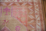 Distressed Oushak rug corner with bubblegum pink blossoms, beige field, and terracotta serrated border.
