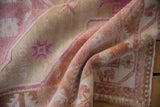 Distressed Oushak rug pile with soft pink, beige, and terracotta tones, showcasing floral motifs.