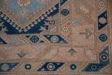 Distressed Melas rug corner: geometric floral border with serrated leaves in peach and blue.