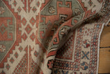 Textural pile of a distressed Oushak rug showcasing ivory, madder red, and dusty blue geometric motifs.