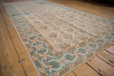 Angled view of a distressed Oushak runner's seafoam green and bronze starburst border design.