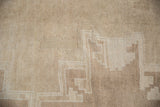 Distressed Oushak carpet with short, even pile showing stepped geometric pattern in beige and ivory.