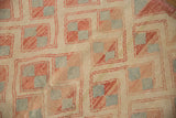 Close-up of distressed Oushak rug showing geometric pinwheel motif in ivory, pale red, and silver.
