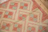 Distressed Oushak rug corner, repeating pinwheel and pawn motifs in pale red, ivory, and blue.