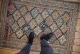 Antique Shirvan rug's intricate stepped lattice pattern, navy, sand, pink hues, and visible pile wear.
