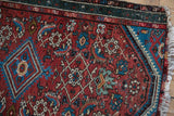 Detail of a Persian Hamadan rug: cherry red field, sky blue Herati design, and tattered edge.