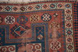 Antique Caucasian rug corner: madder red, indigo blue geometric patterns, visible foundation wear.