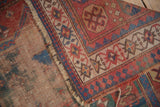Antique Caucasian rug corner showing exposed foundation, red field, geometric border, and safety pin.