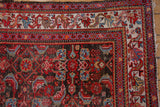 Meandering vine and floral main border on a vintage Hamadan rug corner, with wear visible.