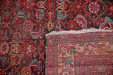 Vintage Hamadan rug close-up, revealing worn red Herati pile and hand-knotted foundation.