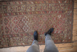 Repeating geometric field and wide floral border on antique Kurdish rug in dusty red, camel hues.