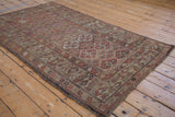 Antique Kurdish rug edge showing dusty wine red floral border, camel panels, and wear to knot heads.