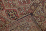 Antique Kurdish rug corner detail: worn pile, visible foundation, dusty red and camel geometric motifs.