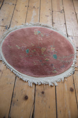 Round Art Deco rug with dusty pink field, delicate floral motifs, and ivory fringe.