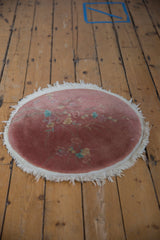 Art Deco round rug close-up: dusty pink field with pale blue, beige floral blossoms and fringe.