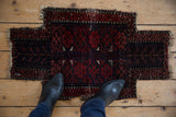 Rich madder red geometric diamond gul motifs on antique Belouch rug with tattered edges.