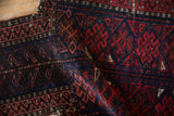 Belouch tribal rug with geometric patterns in navy, madder red, brown, and tattered edge.