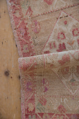 Distressed texture and faded raspberry patterns on the vintage Oushak rug mat's edge.