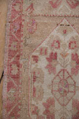 Distressed Oushak rug detail showing raspberry motifs, sand field, worn pile, and exposed foundation.