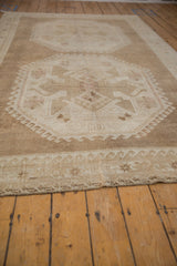 Distressed vintage Oushak carpet: reciprocating wave border, geometric plant design, soft ivory and coffee.