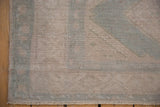 Distressed Oushak rug corner showing muted ivory, pale sage tones, and fringe.