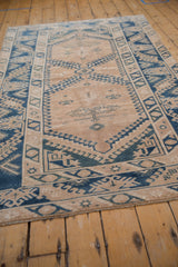 Angled view showing faded cobalt blue geometric motifs and distressed beige texture on a Melas rug.