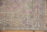 Distressed Oushak rug runner's geometric border, fuchsia pinwheel flowers, and aged pile.