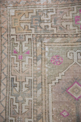 Distressed vintage Oushak rug runner showing geometric border, fuchsia accents on a worn pile.