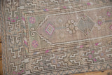 Distressed Oushak rug corner showing geometric border and fuchsia pinwheel flowers.