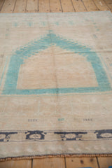 Aqua blue prayer mehrab motif on a distressed beige Oushak rug field.