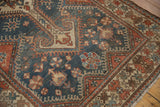 Close-up on the distressed, low-pile texture of a vintage Hamadan rug with geometric designs in blue and red.