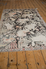 Distressed Qom rug corner with ivory, blush hunting scene, and visible wear.