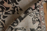 Rolled edge of distressed Qom rug, showing charcoal, ivory, and blush pictorial texture.