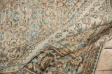 Folds of a distressed Hamadan carpet revealing ivory, beige, and seafoam green Herati patterns.