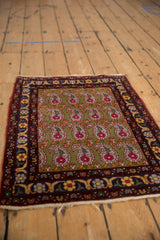 Angled view of a vintage Farahan Sarouk rug with a repeating boteh pattern on a sage green field.