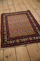 Vintage Farahan Sarouk rug with a repeating paisley design on a sage green field, shown at an angle.