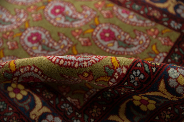 Close-up of a folded vintage Farahan Sarouk rug highlighting the short pile and sage green boteh design.